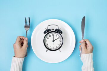 Person holding a knife and form with an alarm clock on a plate in front of them.