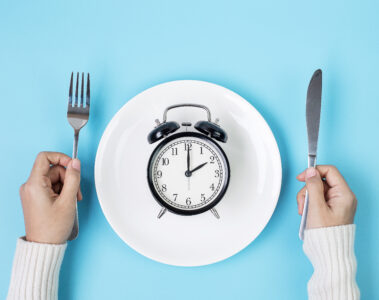 Person holding a knife and form with an alarm clock on a plate in front of them.